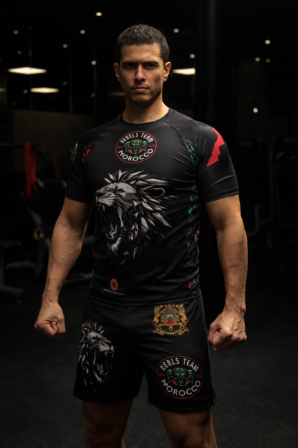 Combattant portant un rashguard et short Moroccan Punch noir style MMA / Muay Thai avec design lion Atlas et logos Rebels Team Morocco dans une salle de sport sombre premium