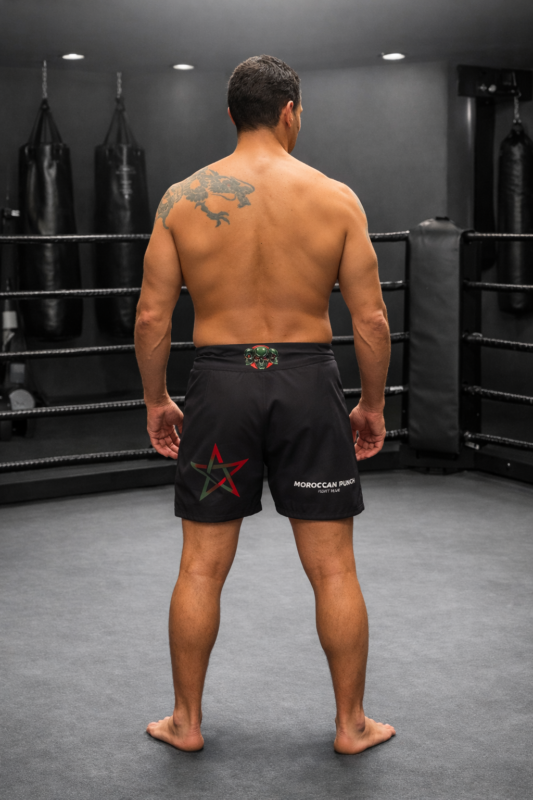 Short MMA Moroccan Punch noir avec design lion Atlas et logo Rebels Team Morocco porté par un athlète dans une salle de sport, idéal pour Muay Thai, Jiu Jitsu, CrossFit et sports de combat.