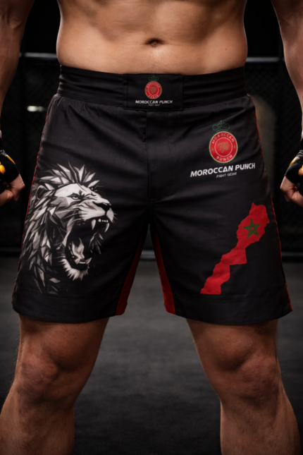 Short de combat Moroccan Punch noir avec lion Atlas et carte du Maroc rouge, porté par un athlète MMA dans une cage d’entraînement, idéal pour Muay Thai, Jiu Jitsu, MMA et CrossFit